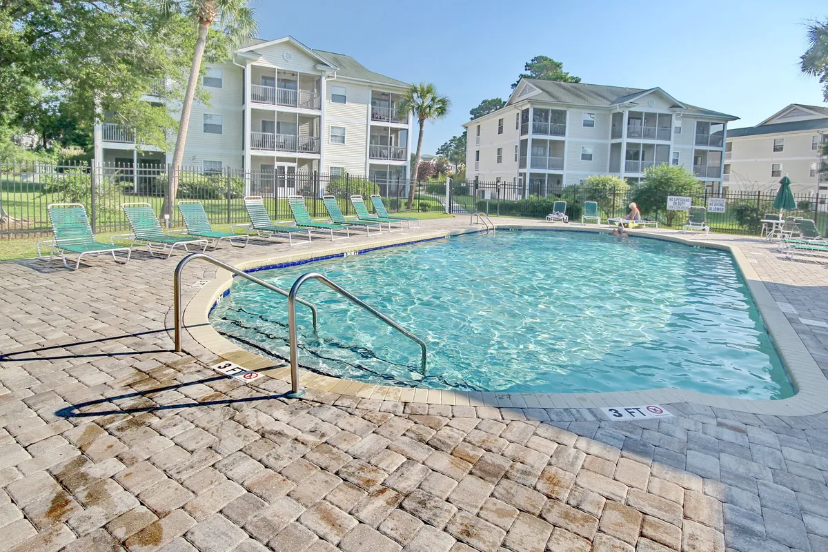 This exterior image features a sparkling swimming pool surrounded by lounge chairs and lush greenery. The inviting blue water is perfect for morning swims or relaxing dips, while the ample seating encourages socializing and sunbathing. The well-maintained landscaping enhances the resort-like ambiance.