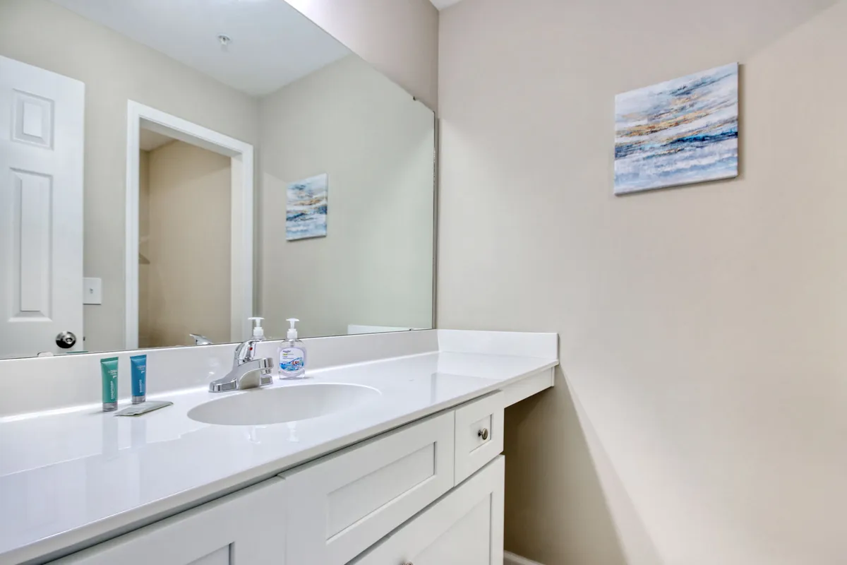 A bright bathroom space with a white vanity, large mirror, and abstract art, basked in soft morning light. The area feels fresh and inviting—perfect for personal routines or a quick refresh.
