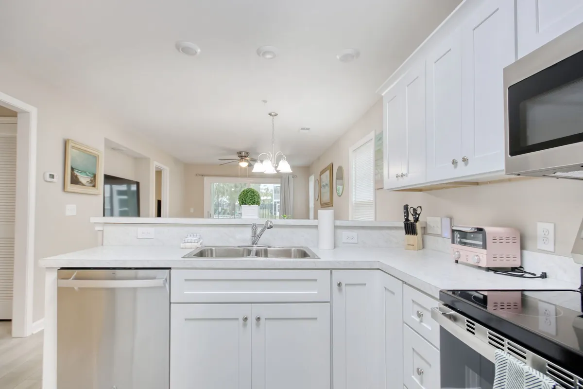 A stylish kitchen island anchors the space, surrounded by stainless steel appliances, a built-in dishwasher, decorative plants, and eye-catching light fixtures. The island also suggests a breakfast bar area, ideal for quick meals or morning coffee chats.
