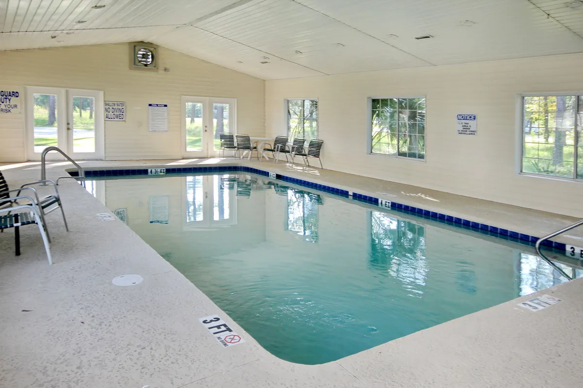 This bright indoor pool scene features shimmering water, comfortable lounge chairs, and large windows streaming with natural light. It conveys a lively yet soothing setting, ideal for both relaxing afternoons and socializing with friends or loved ones.