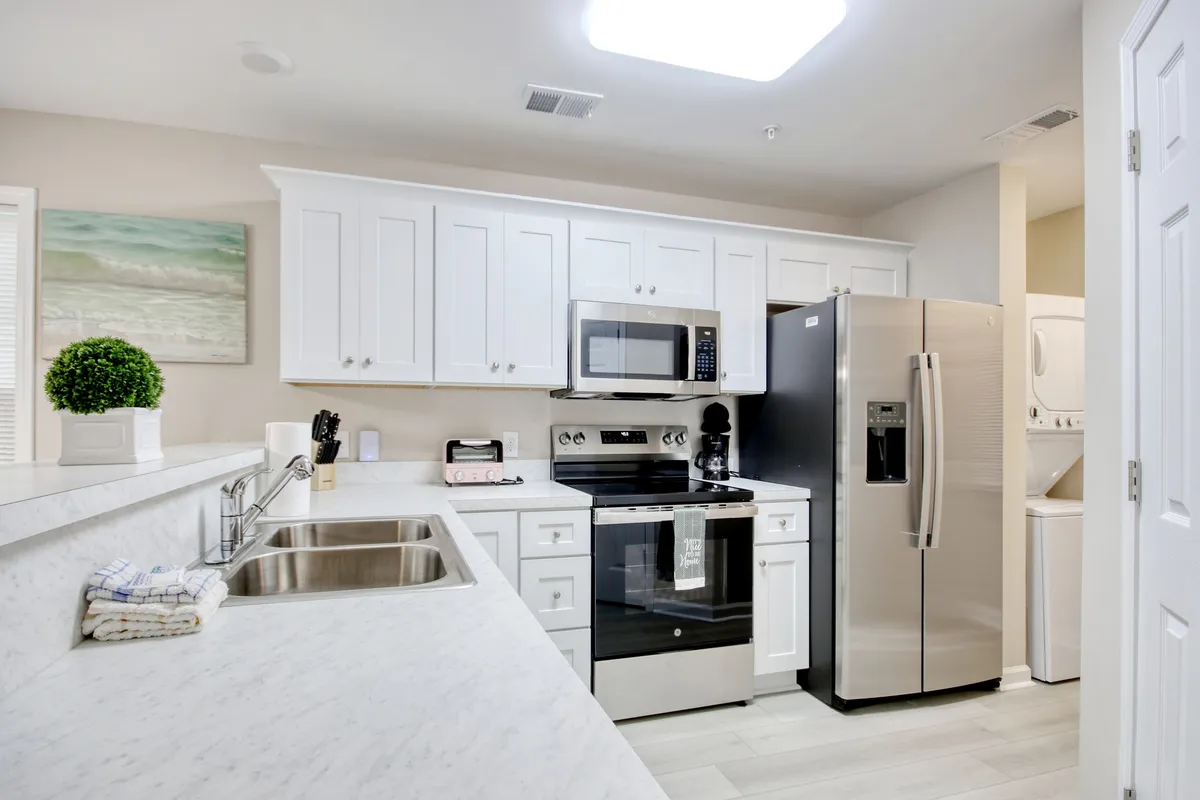 Another angle of the kitchen reveals elegant marble countertops, gleaming stainless steel appliances, white cabinetry, and a decorative plant, suggesting a versatile space equally suited for intimate dinner parties or family recipe nights.