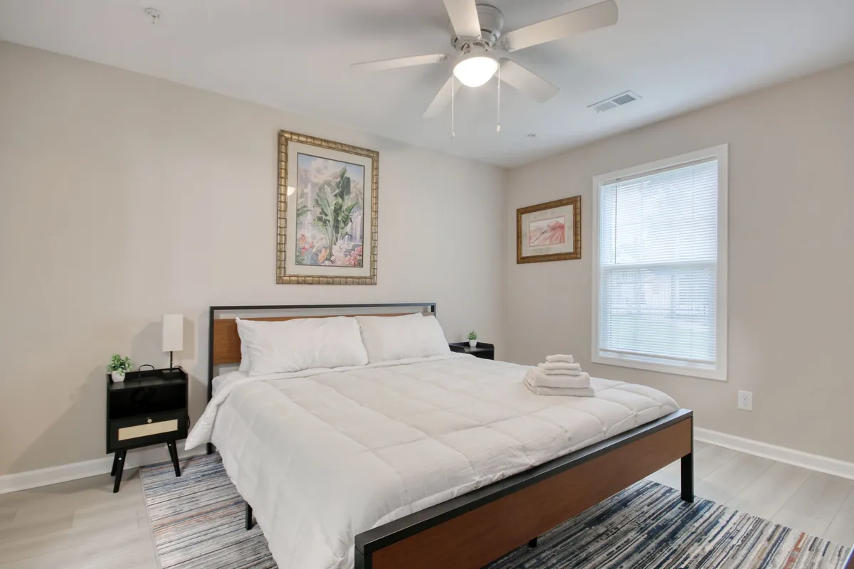 A peaceful bedroom with a cozy bed, soft bedding, elegant wall art, and a nightstand, awash in gentle natural light. The space feels tranquil and perfect for unwinding after a long day.