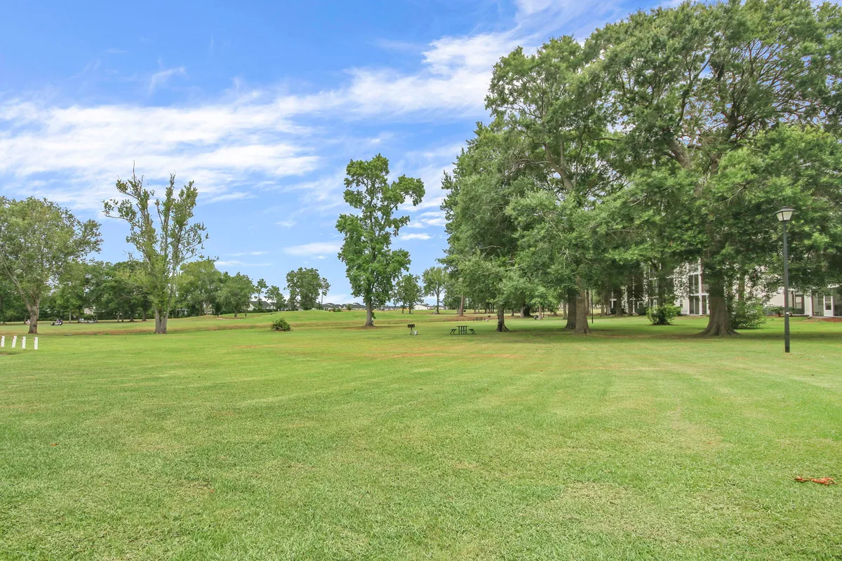 This exterior image showcases an expansive green lawn framed by tall trees, with benches and light posts suggesting a peaceful outdoor environment. The open space evokes the feeling of being near a golf course, with the well-kept grass and natural surroundings ideal for outdoor leisure and relaxation.