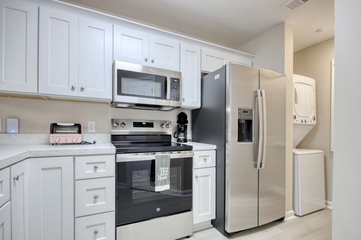 This image shows a bright, contemporary kitchen with stainless steel appliances, white cabinetry, generous countertop space, and a neatly folded kitchen towel with friendly text. The setting is clearly staged for cooking and baking, but also feels welcoming for family gatherings and casual conversations.